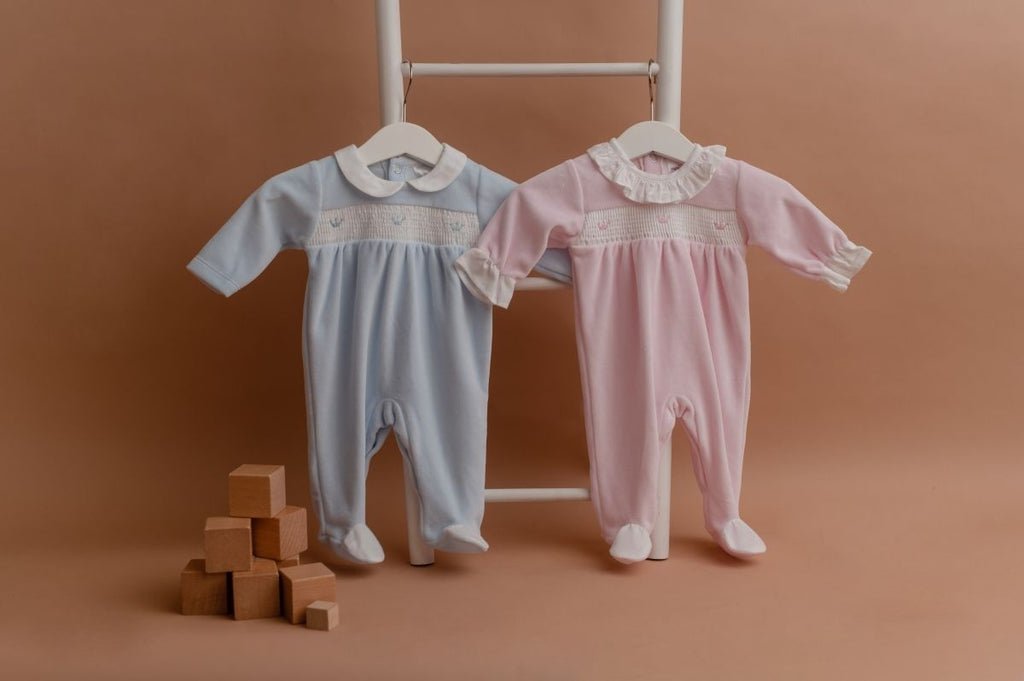 Babygrows bordados em azul e em rosa, pendurados numa escada