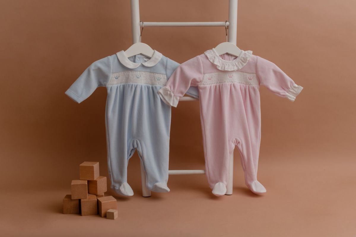 Babygrows bordados em azul e em rosa, pendurados numa escada