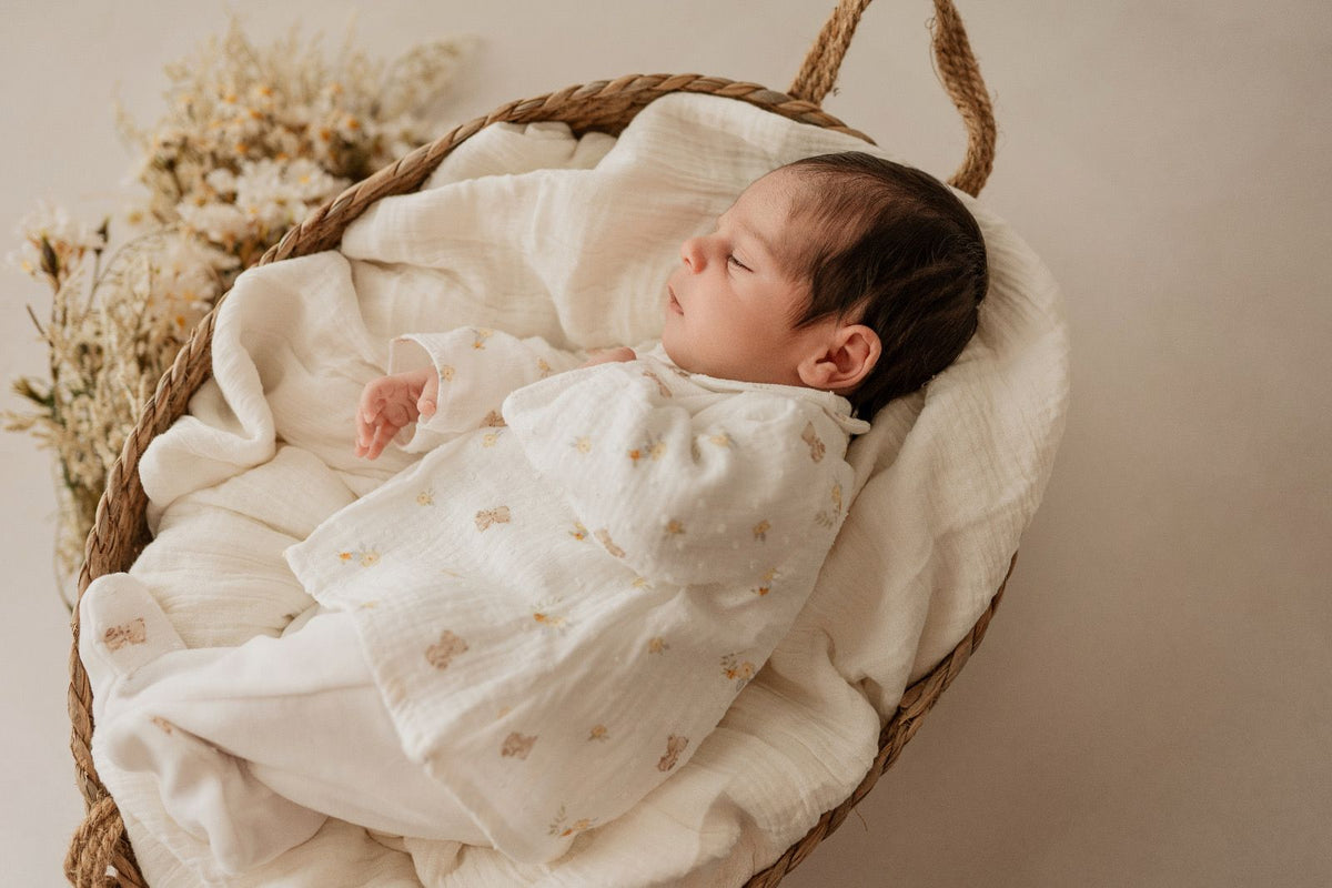 Bebé com o babygrow creme de túnica com ursinhos e flores amarelas