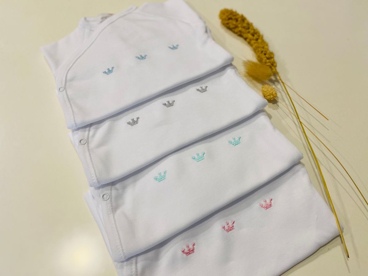 Bodies brancos cruzados com coroinhas bordadas; à venda em rosa e em azul-bebé